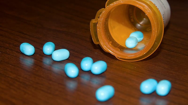 A row of amber prescription vials with white caps on a counter, one open beside a small measuring tray